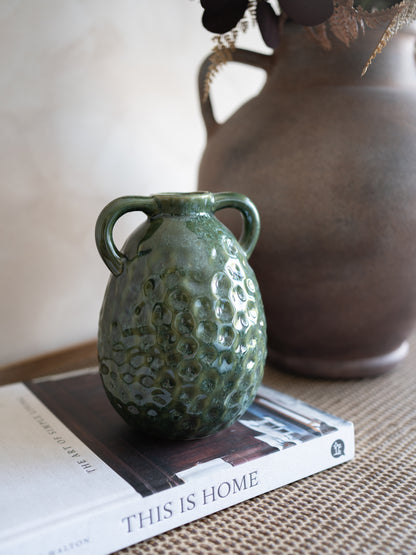 Green textured vase on a book with a brown vase in the background
