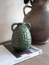 Green textured vase on a book with a brown vase in the background