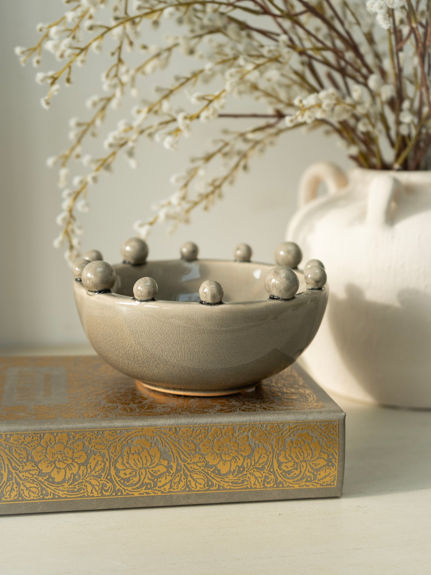 Decorative ceramic bowl with spherical elements on a decorative box with floral patterns, against a neutral background.