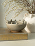 Decorative ceramic bowl with spherical elements on a decorative box with floral patterns, against a neutral background.