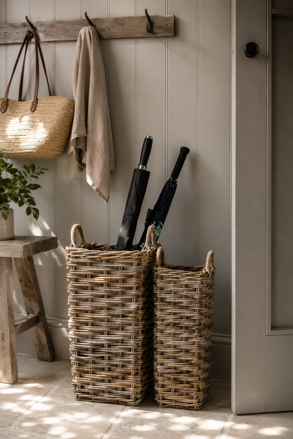 Wicker basket with umbrellas and a bag on a wooden stool against a wall.