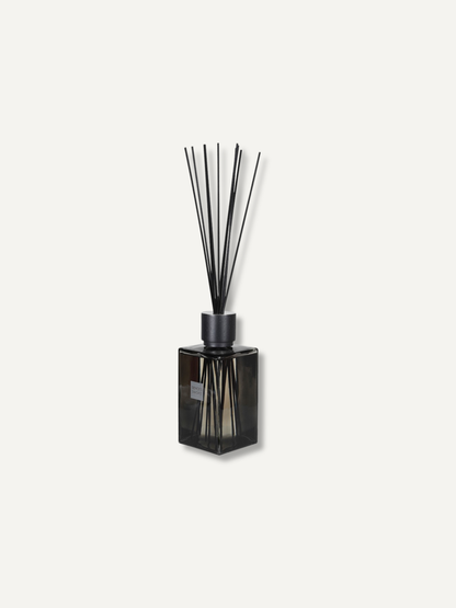 A reed diffuser with a dark glass bottle and black reeds, centered on a light off-white background.