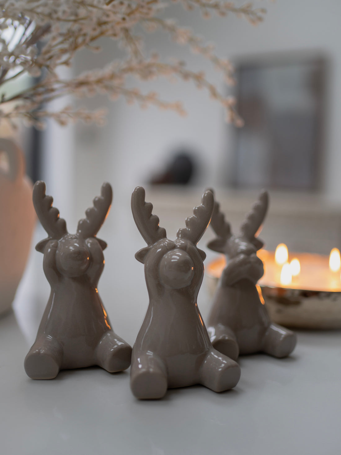 Three grey deer figurines on a surface with a blurred background