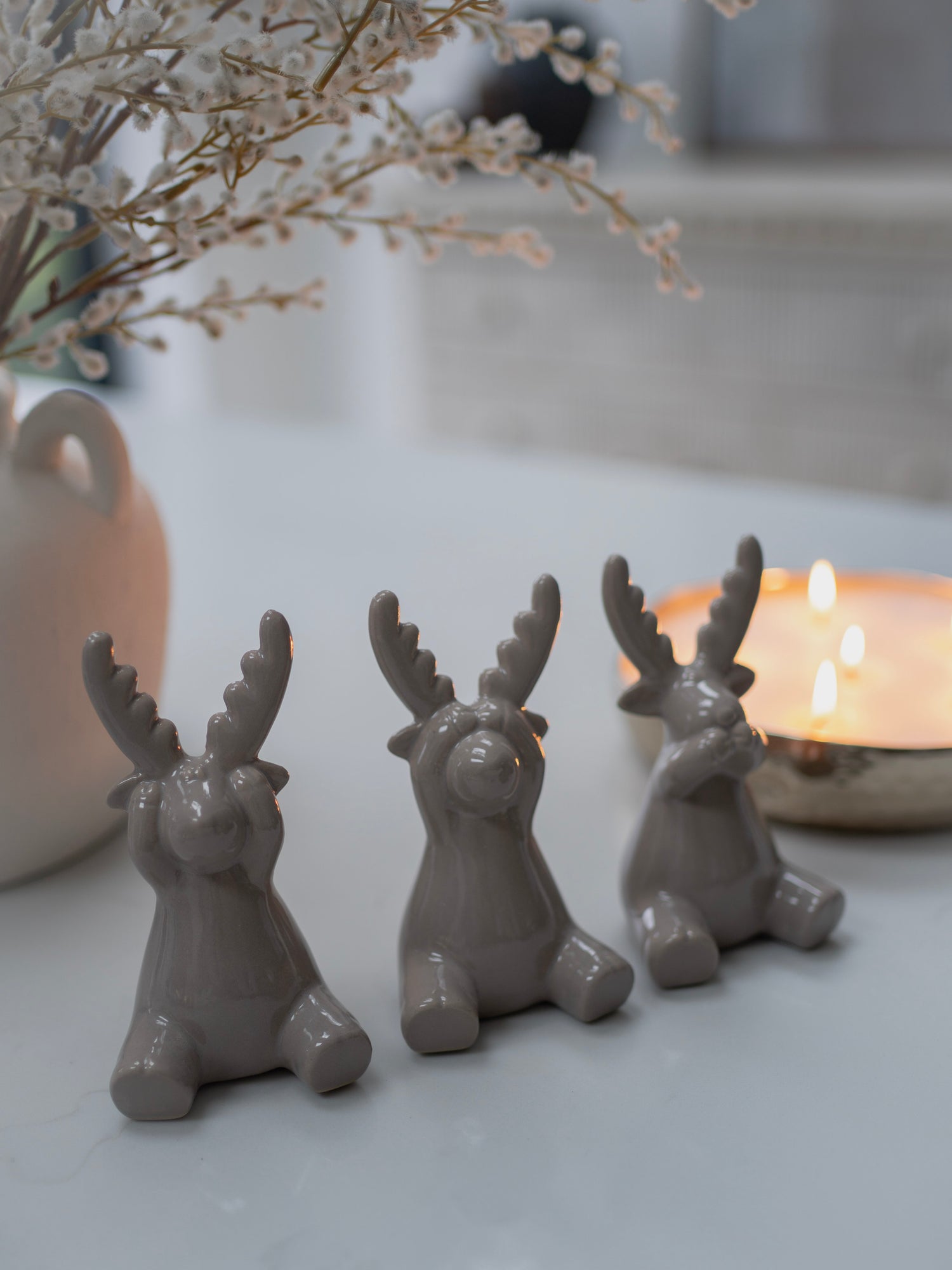 Three grey reindeer figurines on a surface with a blurred background
