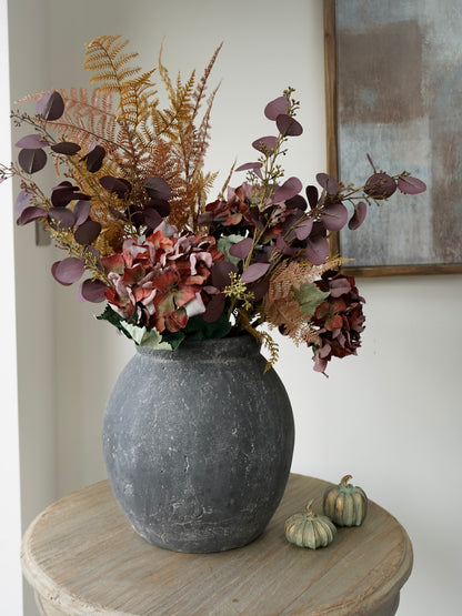 dark charcoal vase with faux dried brown hydrangea, burgundy eucalyptus bracken with little mini pumpkins on round wooden table