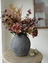 dark charcoal vase with faux dried brown hydrangea, burgundy eucalyptus bracken with little mini pumpkins on round wooden table