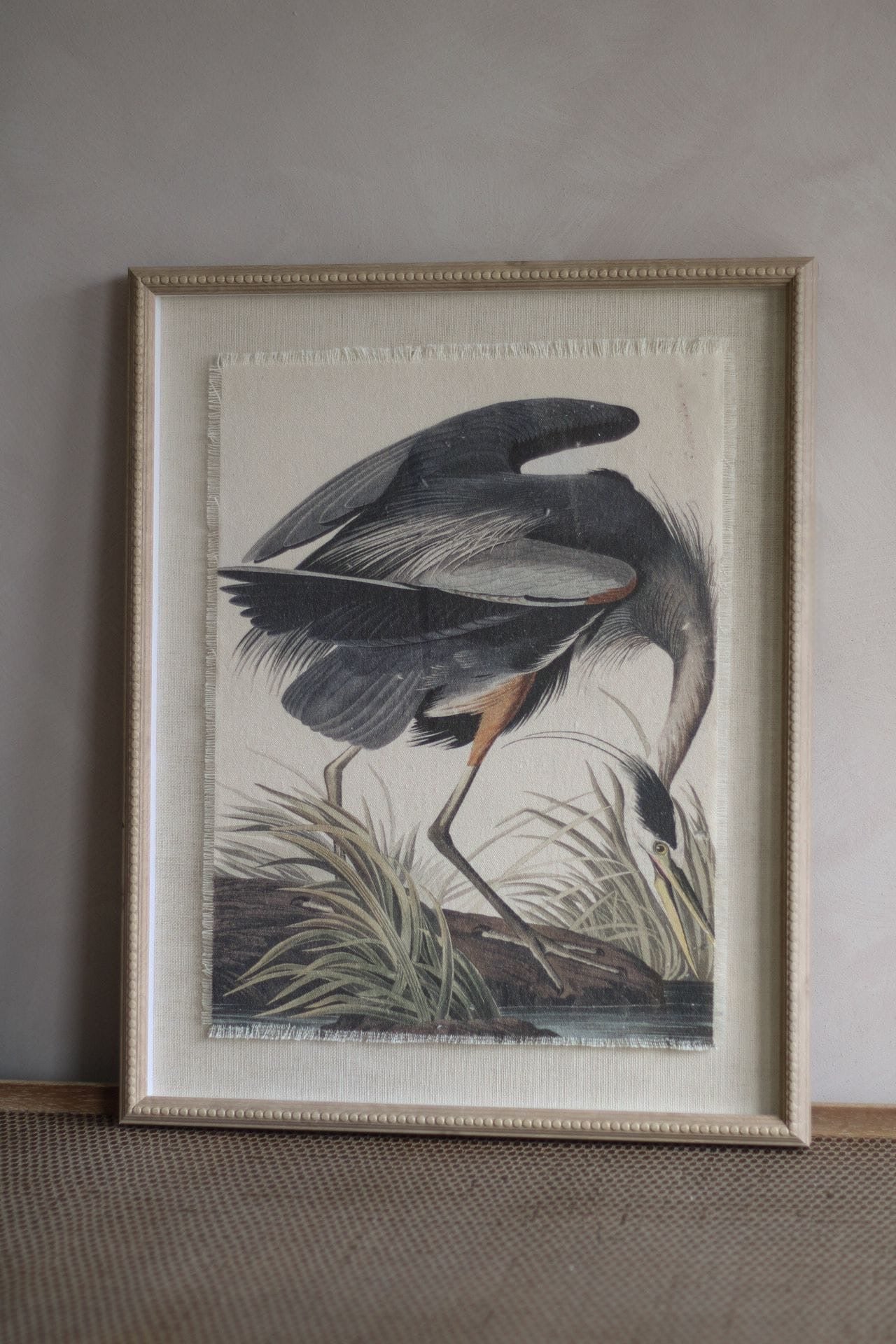 Framed artwork of a bird in a natural setting on a neutral wall.