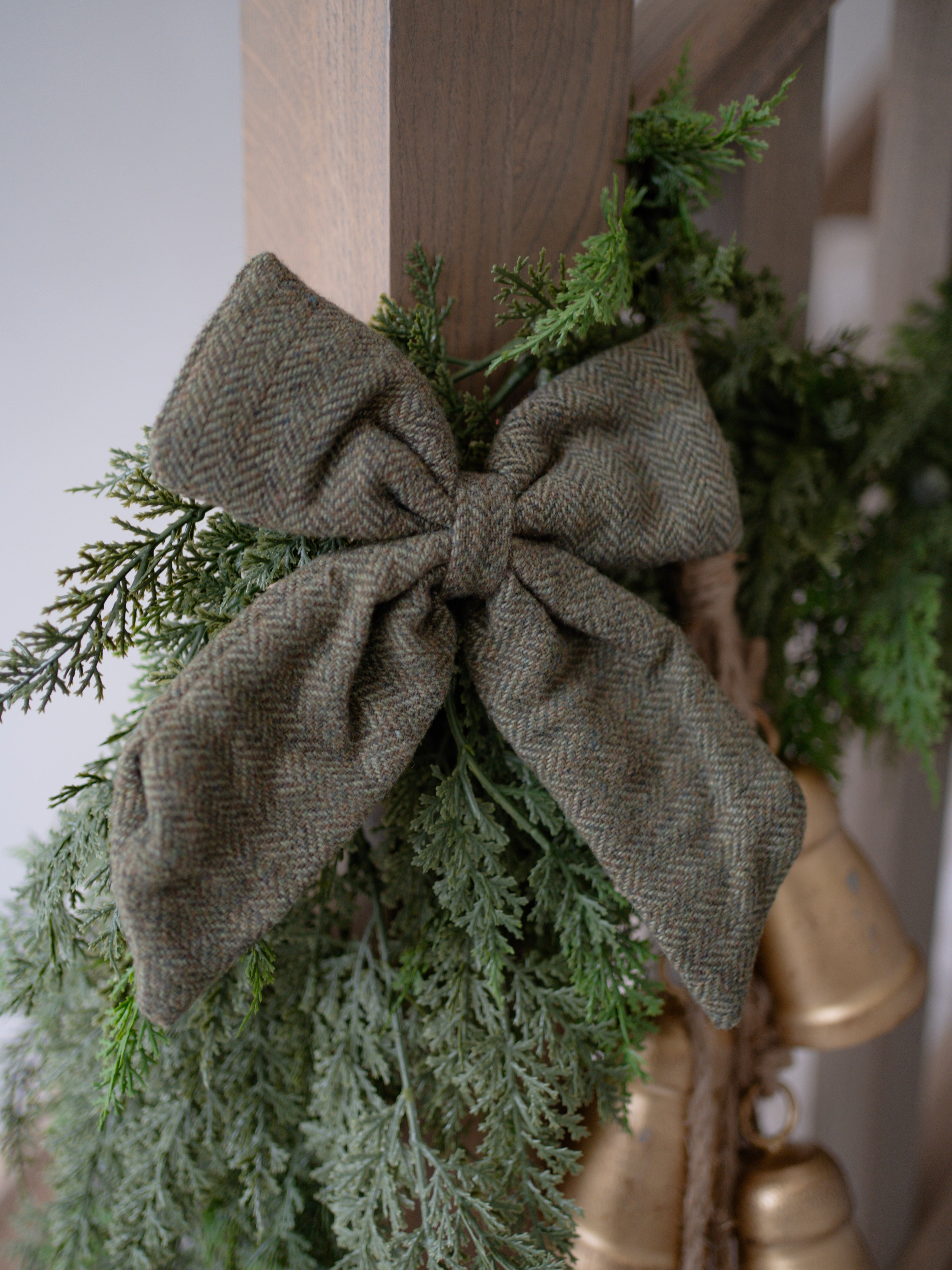 Decorative wreath with greenery and a green herringbone bow on a wooden door.