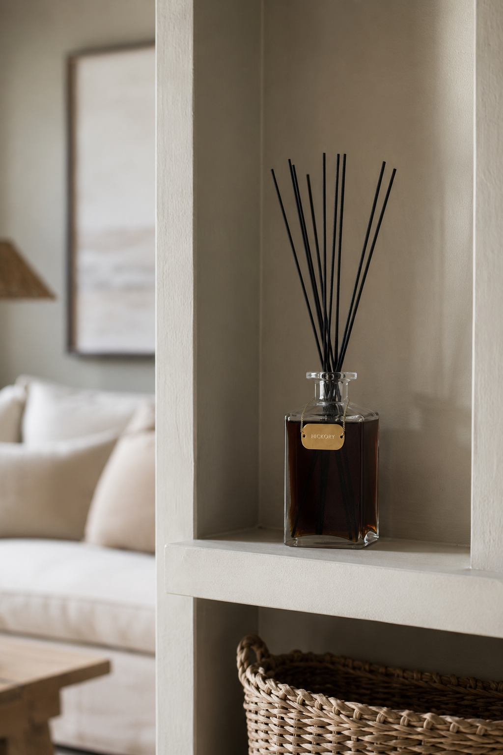 A reed diffuser bottle with black reeds sits on a built-in shelf in a neutral-toned interior setting.
