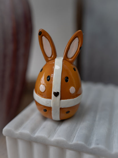 Small ceramic rabbit figurine with a white band on a textured surface