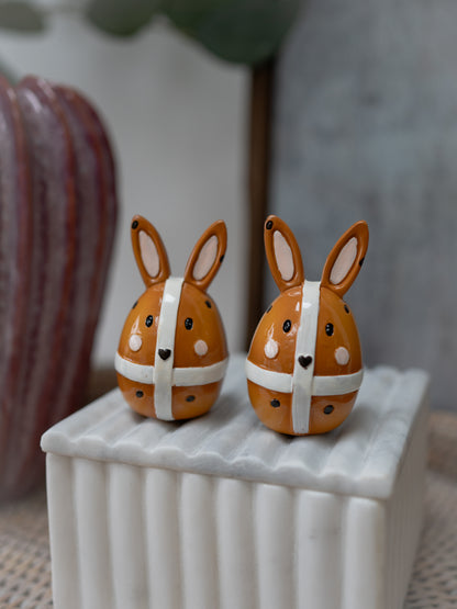 Two decorative bunny figurines with polka dot ribbons on a white surface.