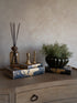 Decorative items including a diffuser, candles, and a plant on a wooden surface with a neutral background.