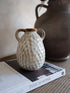 Small textured ceramic vase on a book with a larger brown vase in the background.