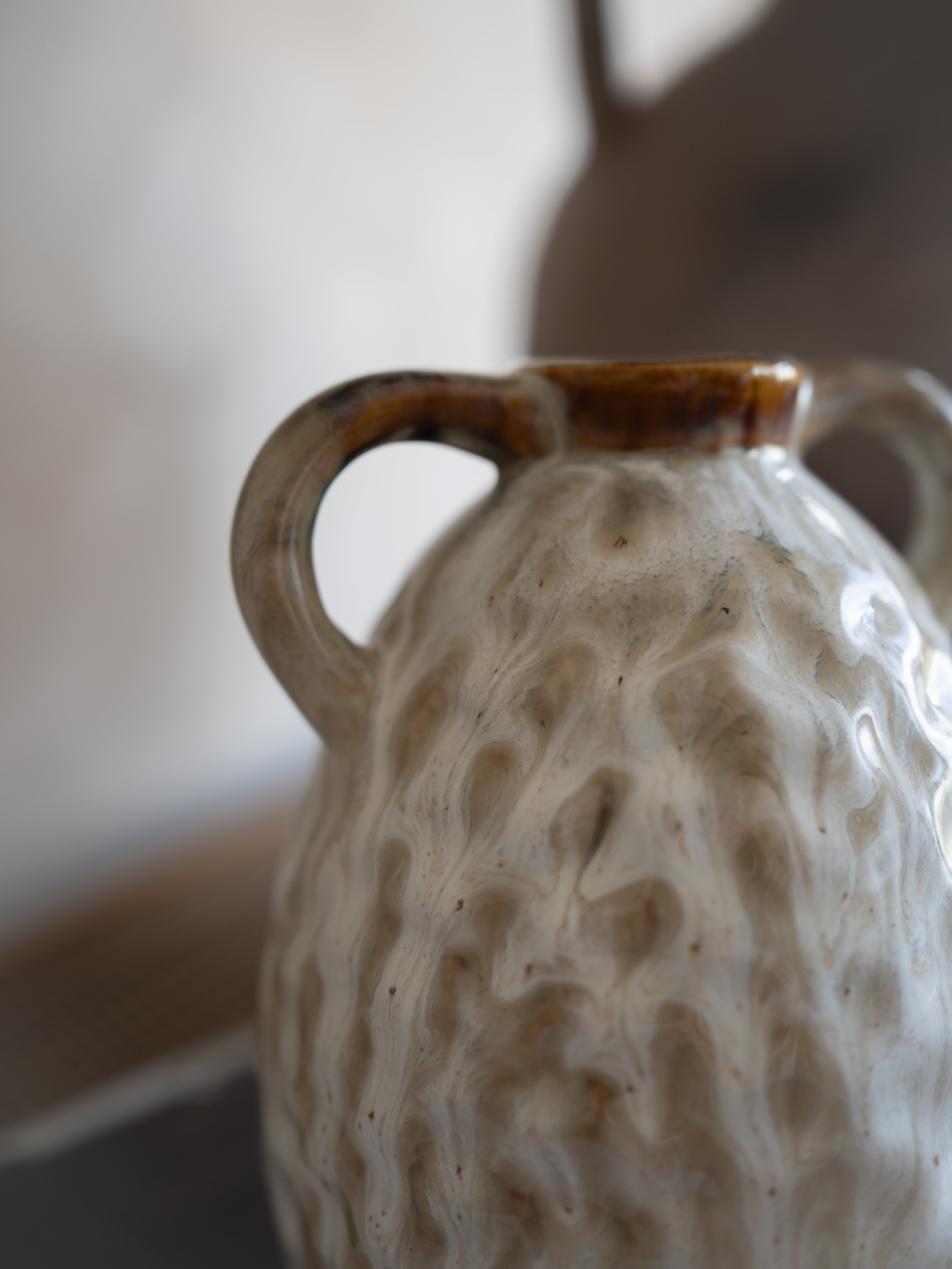 Textured ceramic vase with a handle on a neutral background
