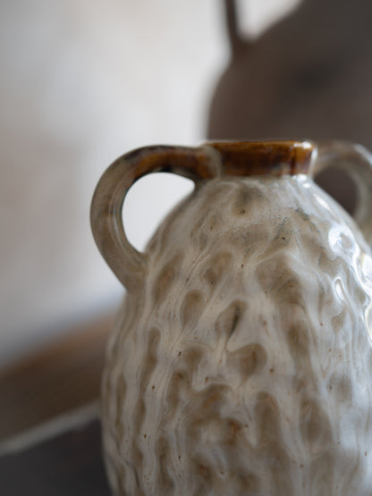 Textured ceramic vase with a handle on a neutral background