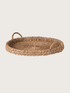 Round woven tray with handles on a light beige background