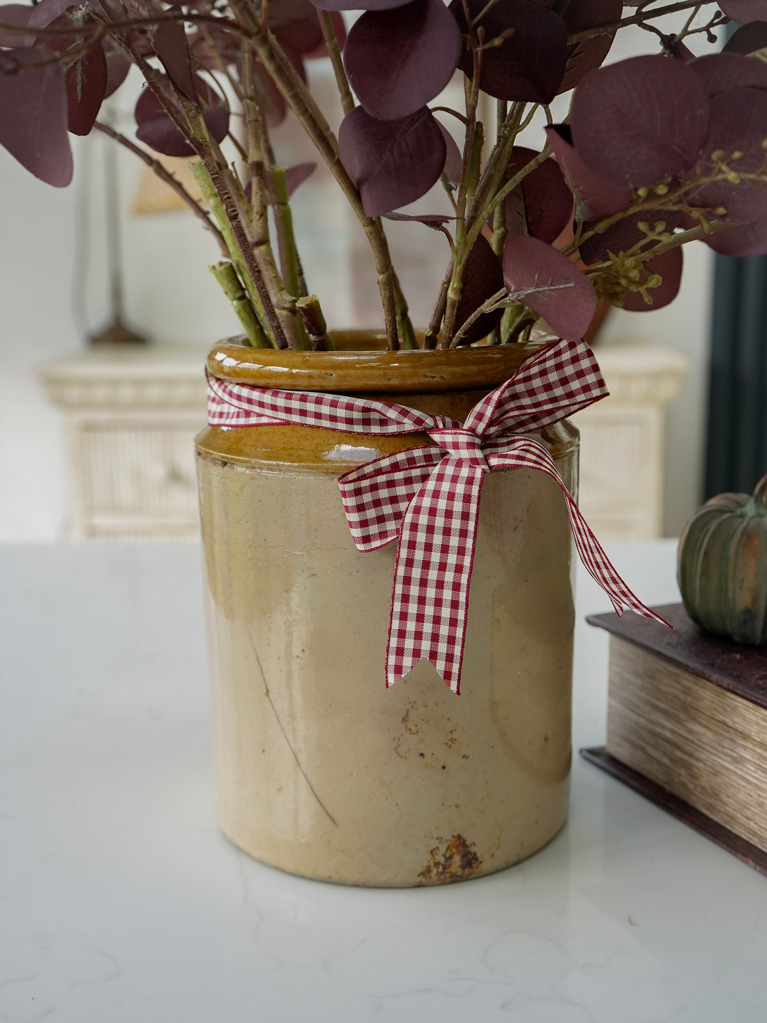 Decorative vase with a checkered ribbon and plants on a white surface