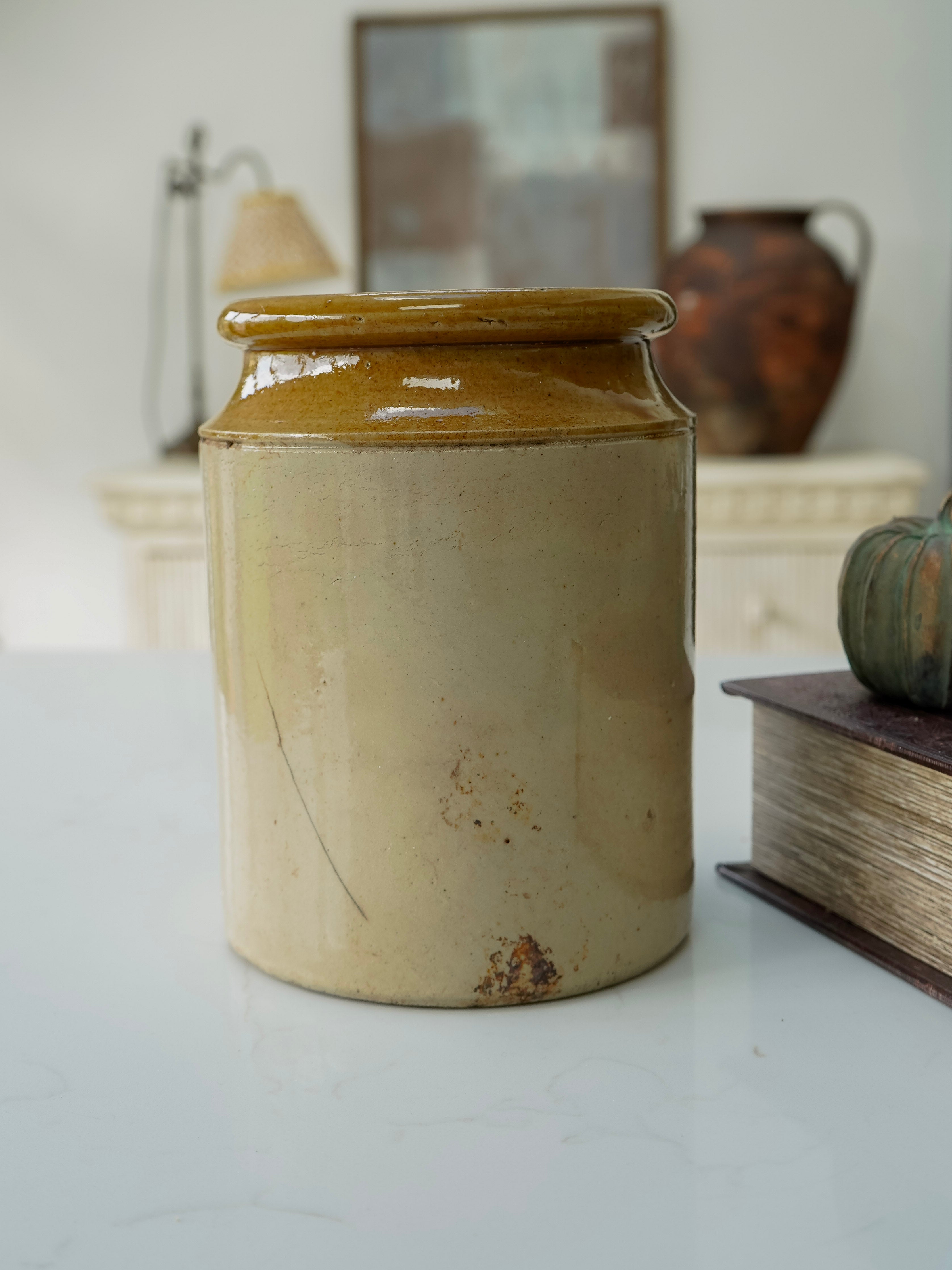 Beige ceramic jar with a lid on a white surface, with a blurred background