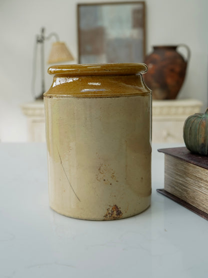 Beige ceramic jar with a lid on a white surface, with a blurred background