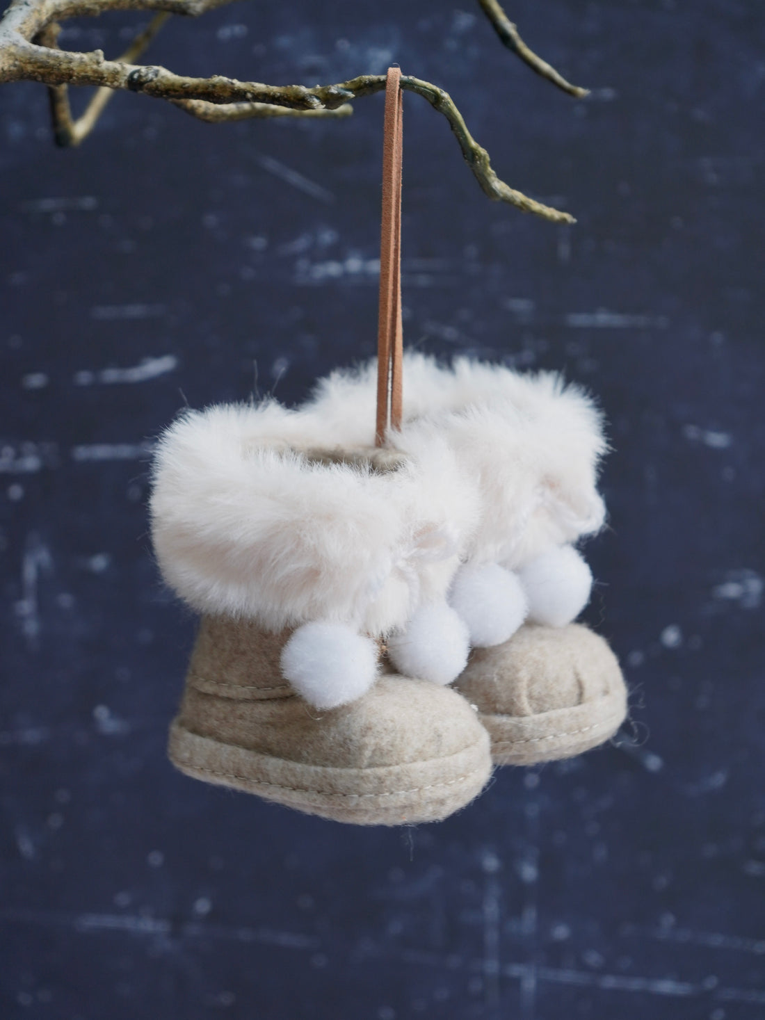 Decorative boot ornaments with fur and white balls hanging from a branch against a dark background.
