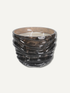 A dark brown and black textured glass candle holder with a wavy, ribbed design, containing a white wax candle, set against a plain off-white background.