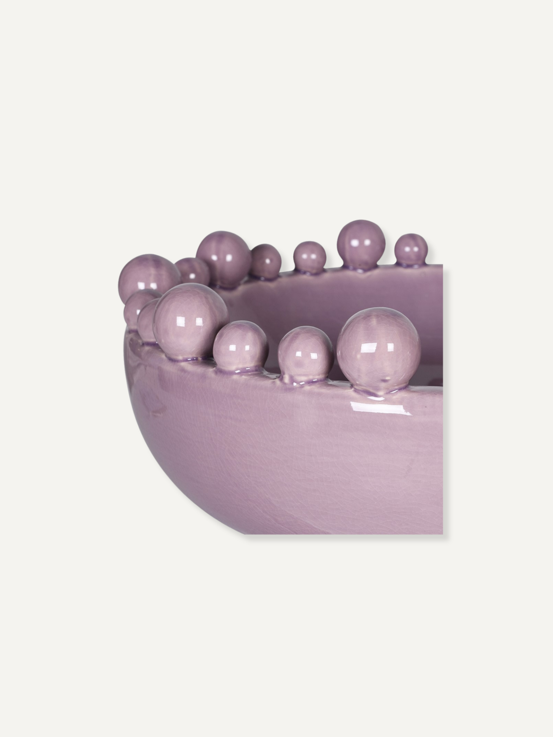 A close-up of a glossy lavender-purple bowl or planter with a row of matching decorative beads along the rim, shown against a plain light beige background.