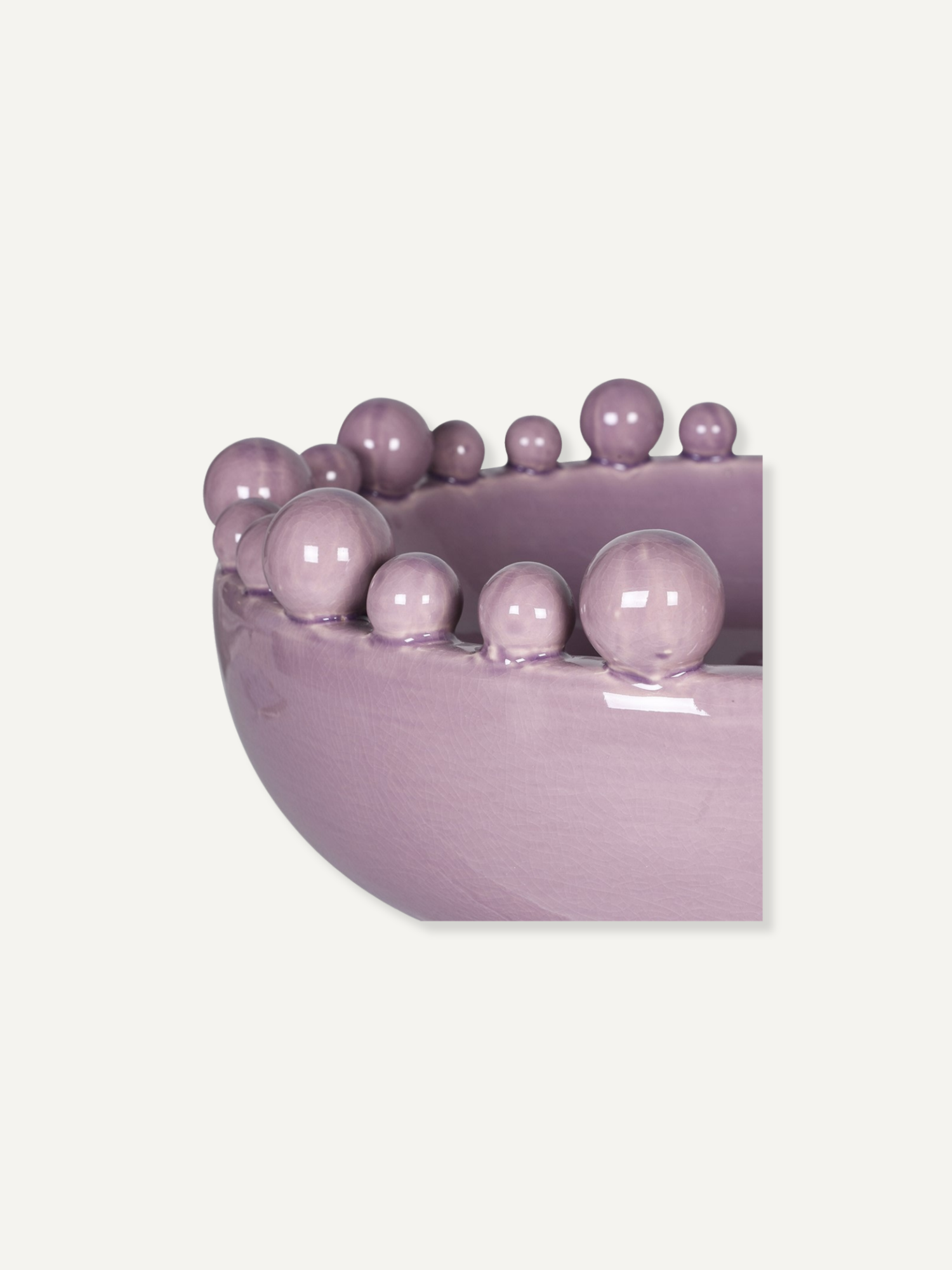 A close-up of a glossy lavender-purple bowl or planter with a row of matching decorative beads along the rim, shown against a plain light beige background.