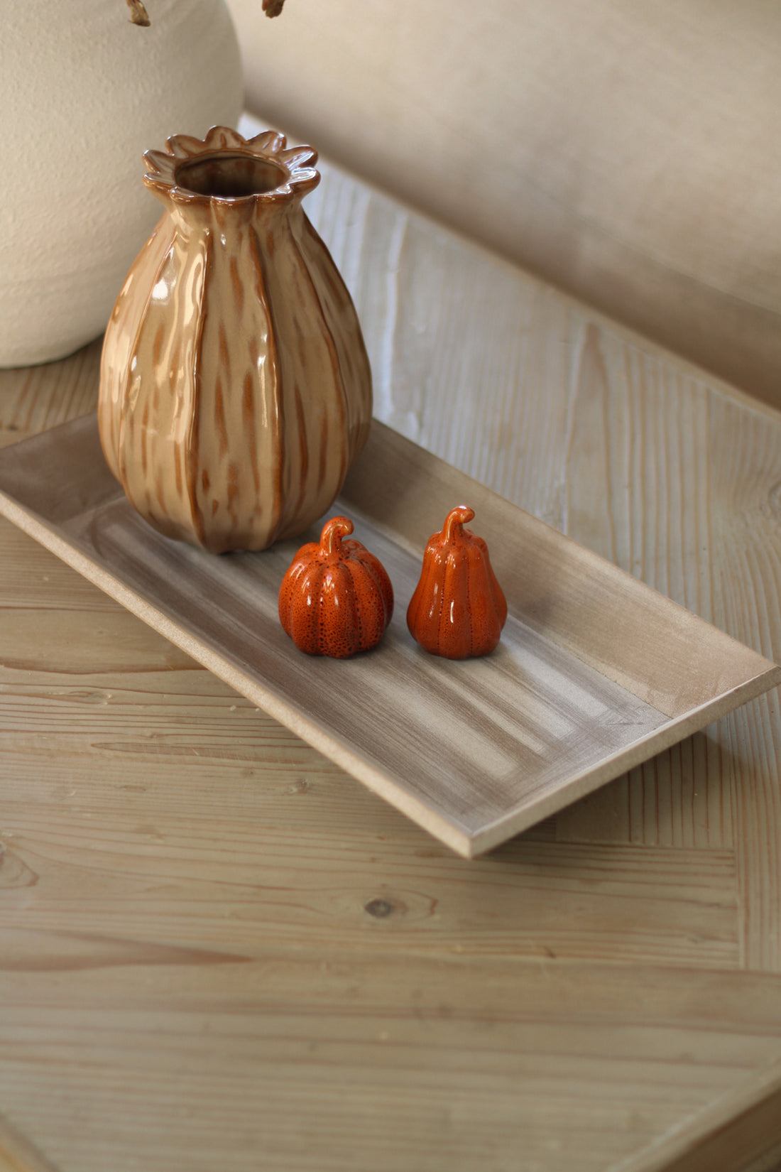 Decorative ceramic vase and small orange pumpkins on a wooden tray.