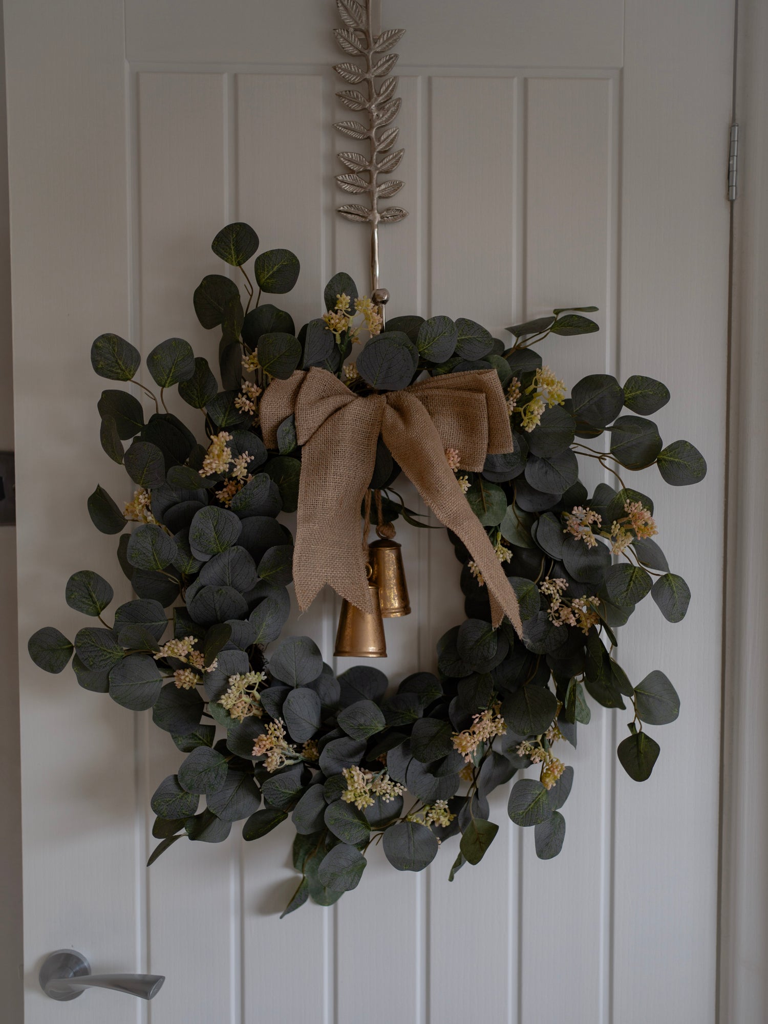 Green wreath with a burlap bow and gold bells on a white door