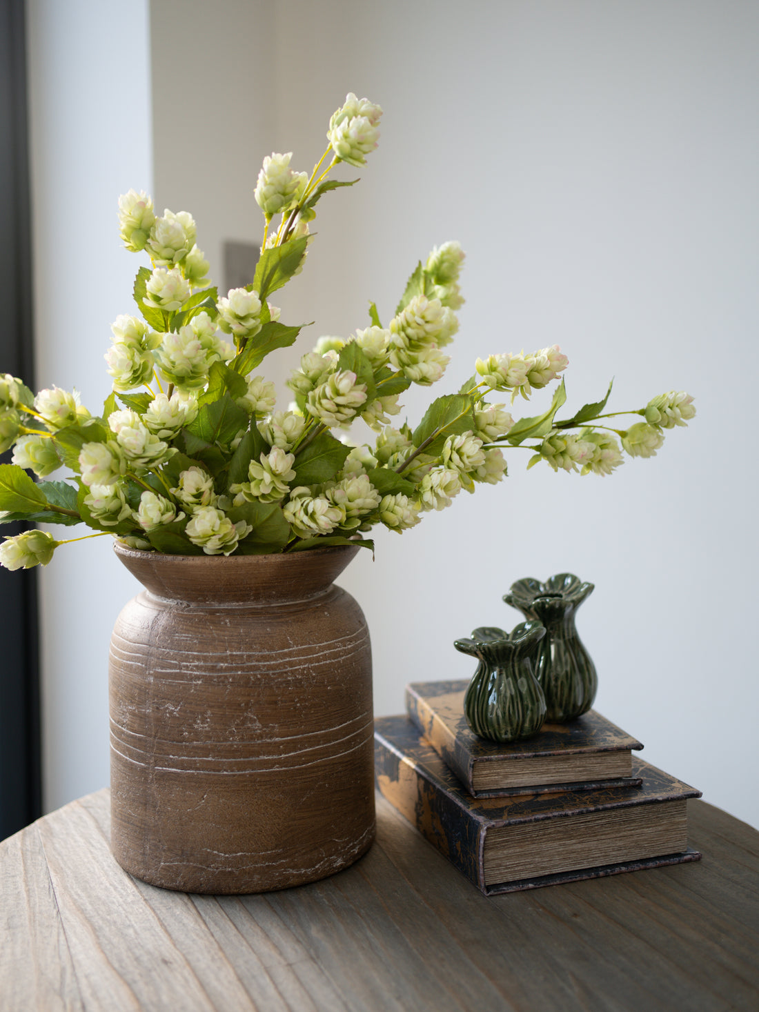 Luxury Faux Green Hops Spray in brown vase with small bud vases on stack of books 
