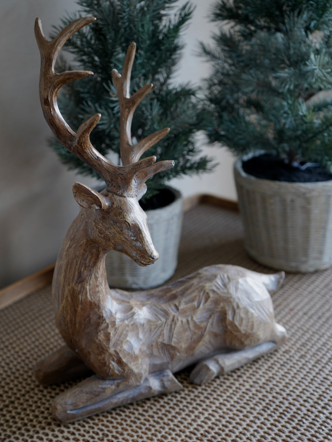 Wooden deer figurine on a textured surface with plants in the background