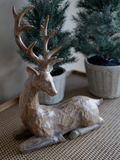Wooden deer figurine on a textured surface with plants in the background