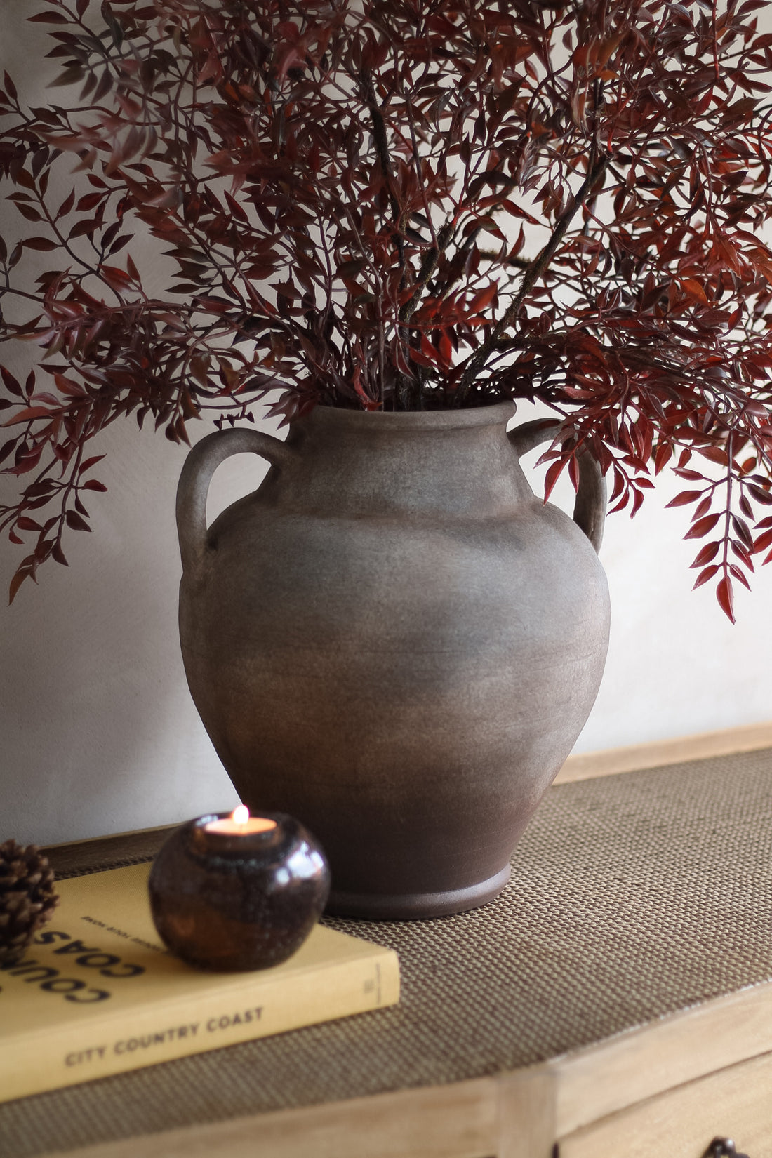 Decorative vase with branches on a table next to a candle and book