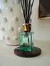 A Senses Marrakesh reed diffuser bottle with a translucent green glass body, a shiny gold cap, and black reeds, resting on a round dark coaster.