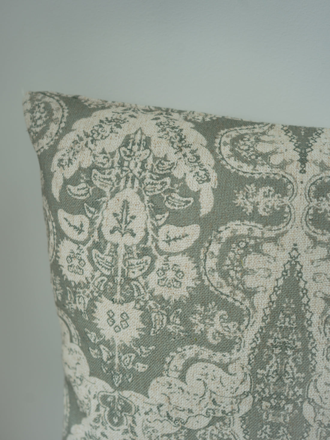 A close-up of a decorative throw cushion featuring an intricate damask pattern in muted sage green and cream.