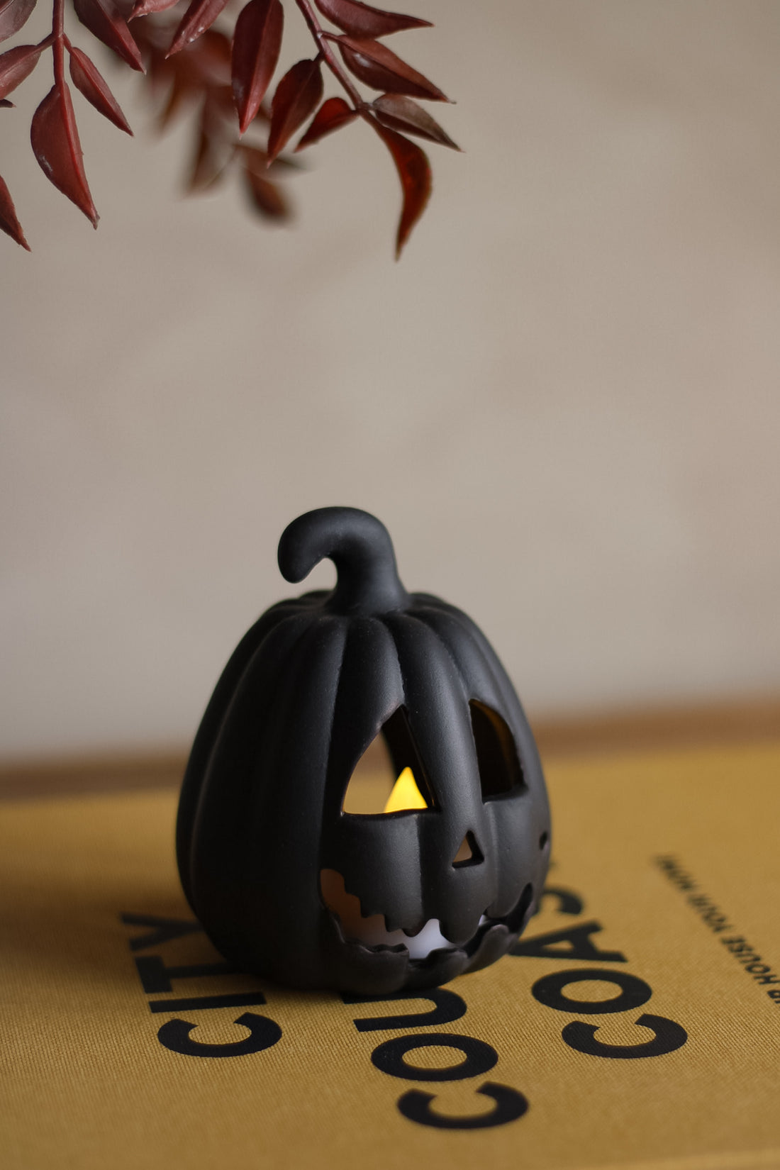 Black ceramic pumpkin with a lit candle inside on a beige surface.