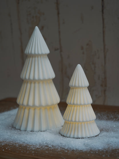 Two white ceramic Christmas trees on a wooden surface with a snowy background.