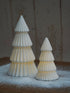 Two white ceramic Christmas trees on a wooden surface with a snowy background.