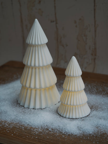 Two white ceramic Christmas trees on a wooden surface with a snowy effect.