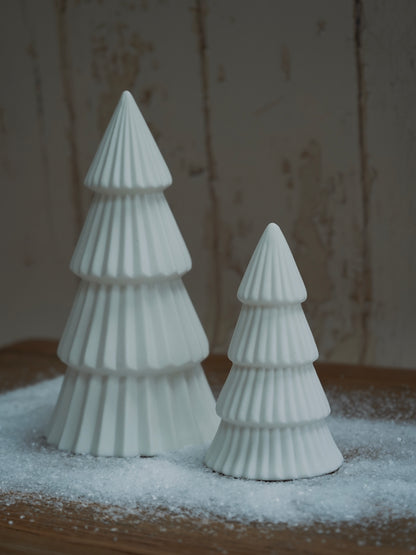 Two white ceramic Christmas trees on a wooden surface with a snowy background