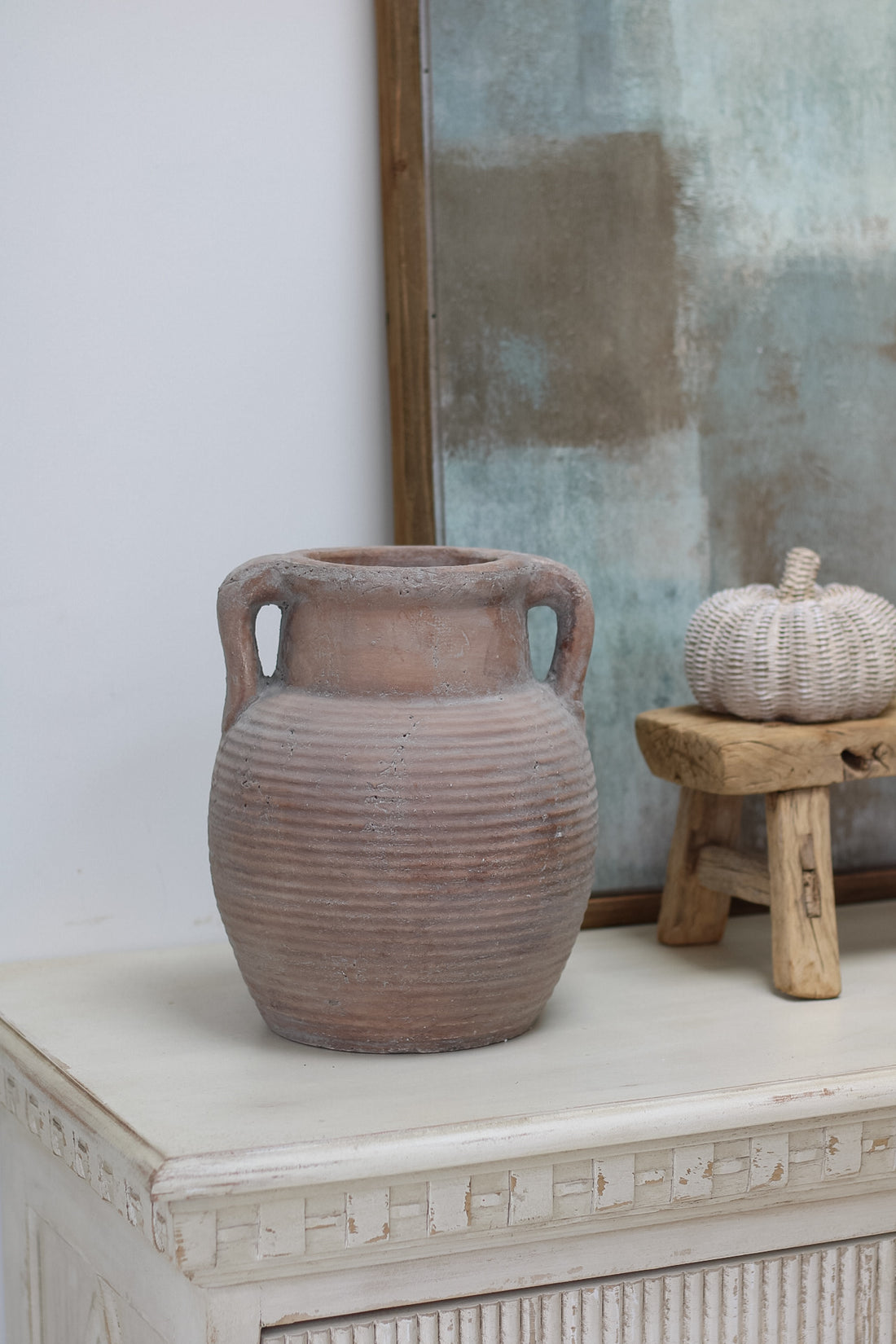 Terracotta vase on a white surface with a textured wall in the background