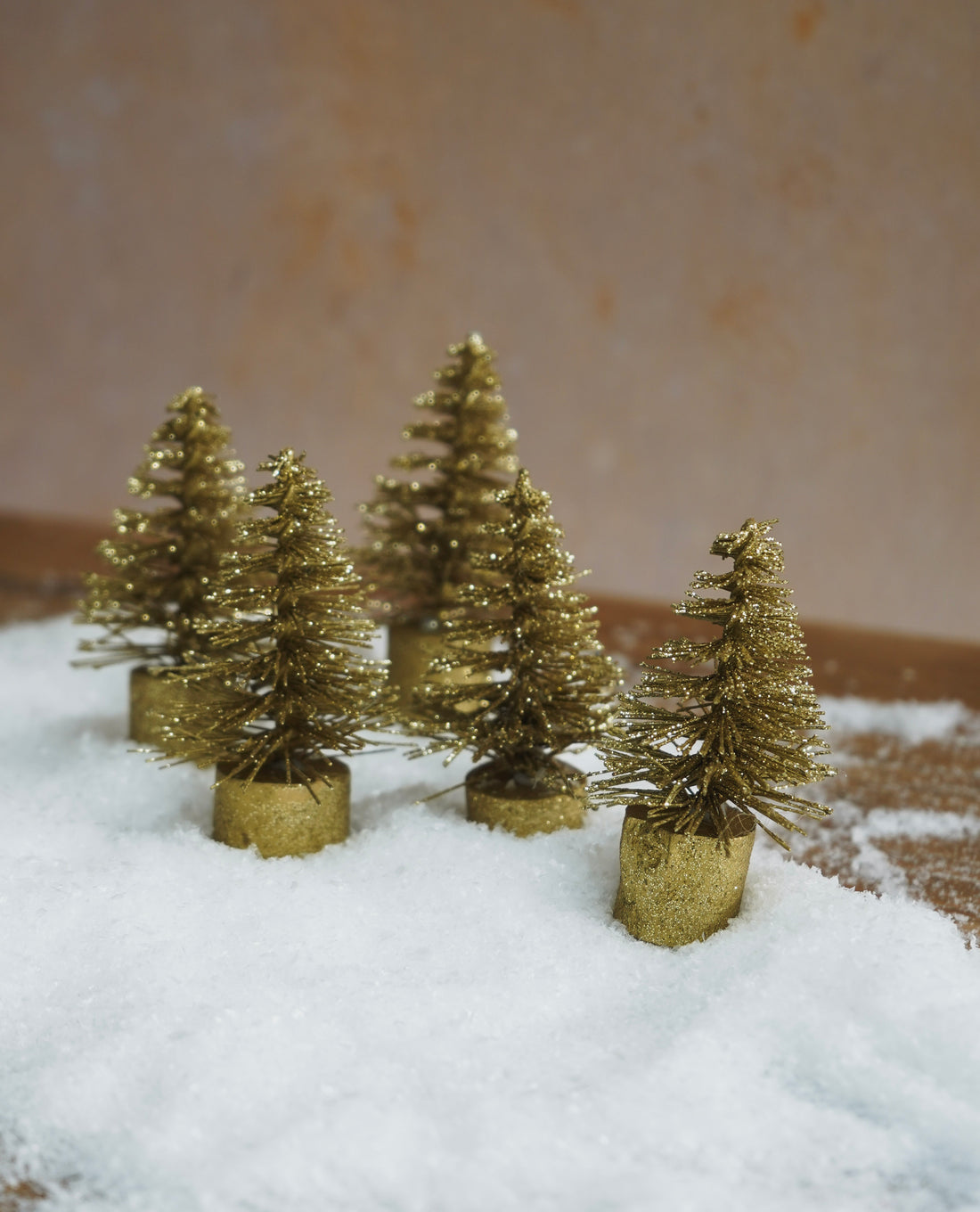 Gold Christmas trees on a snowy surface with a beige background