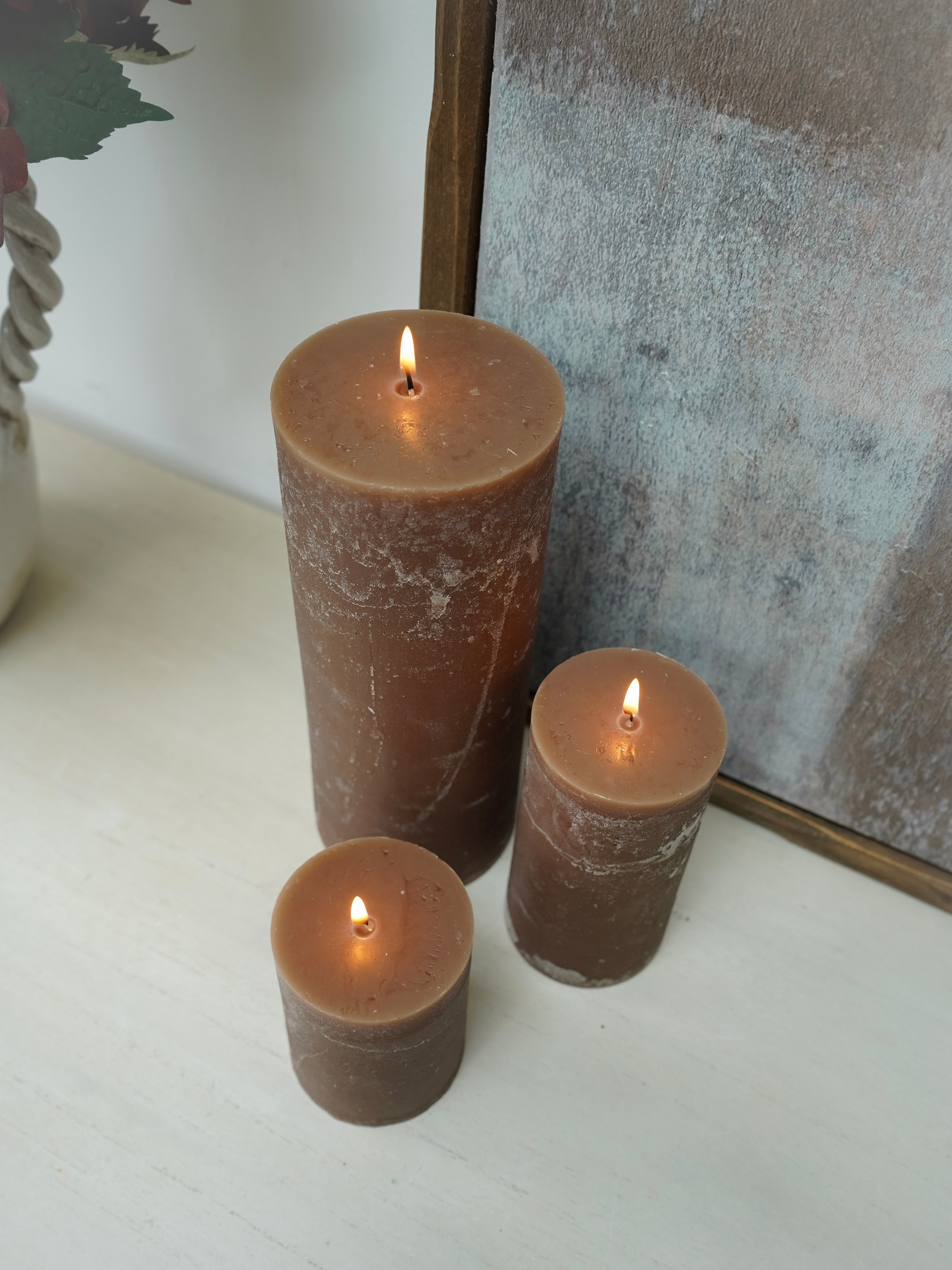 Three brown pillar candles of different sizes on a white surface with a blurred background