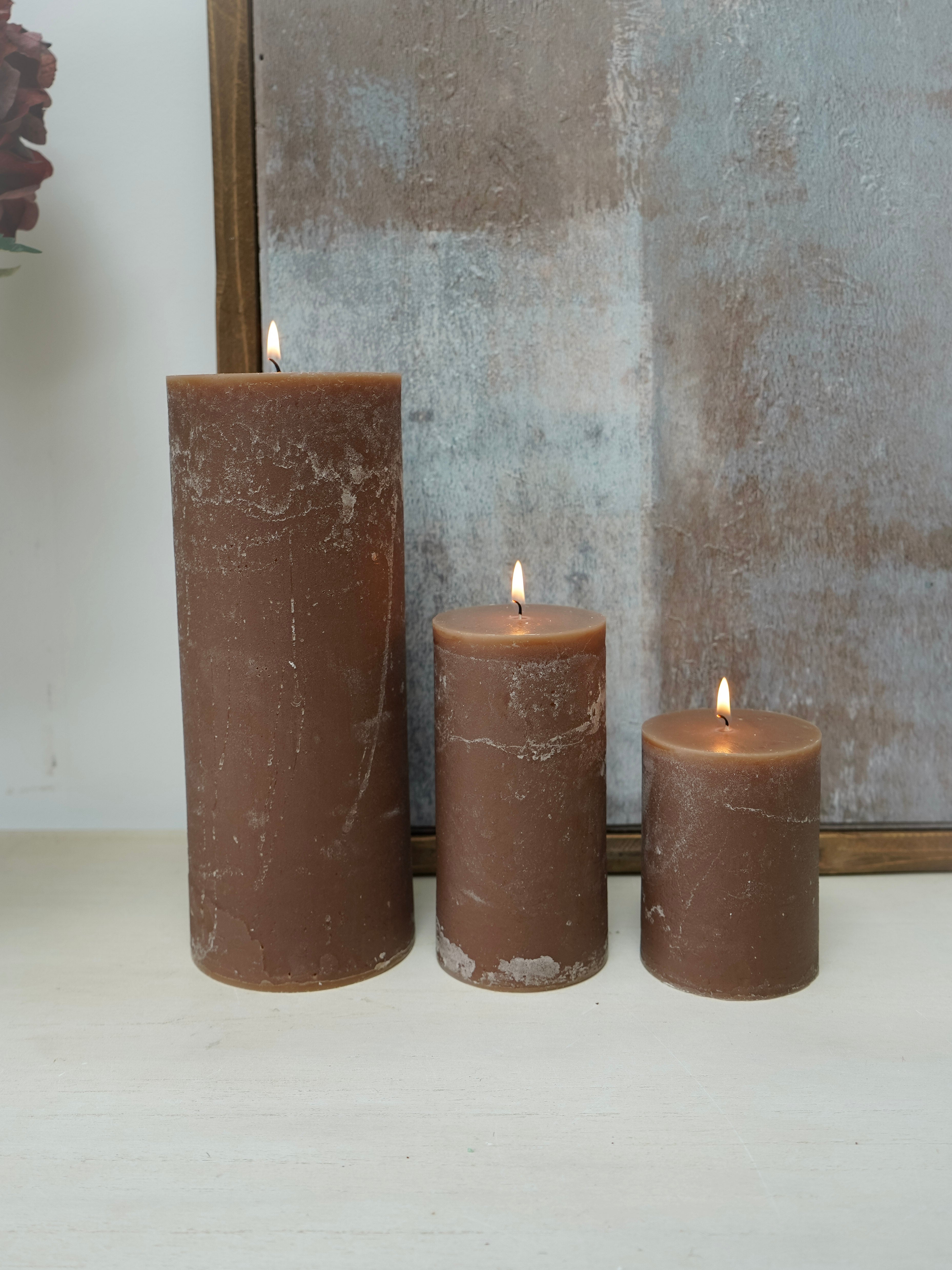 Three brown pillar  candles with a mirror in the background