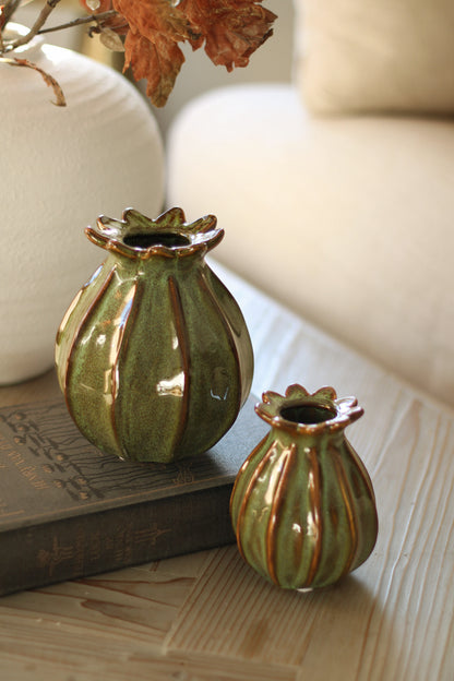 Two green ceramic poppy head vases with brown stripes on a wooden surface.