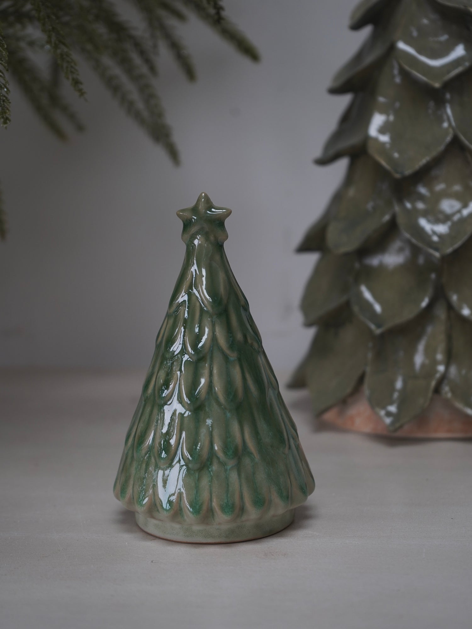 Green ceramic Christmas tree ornament on a neutral background