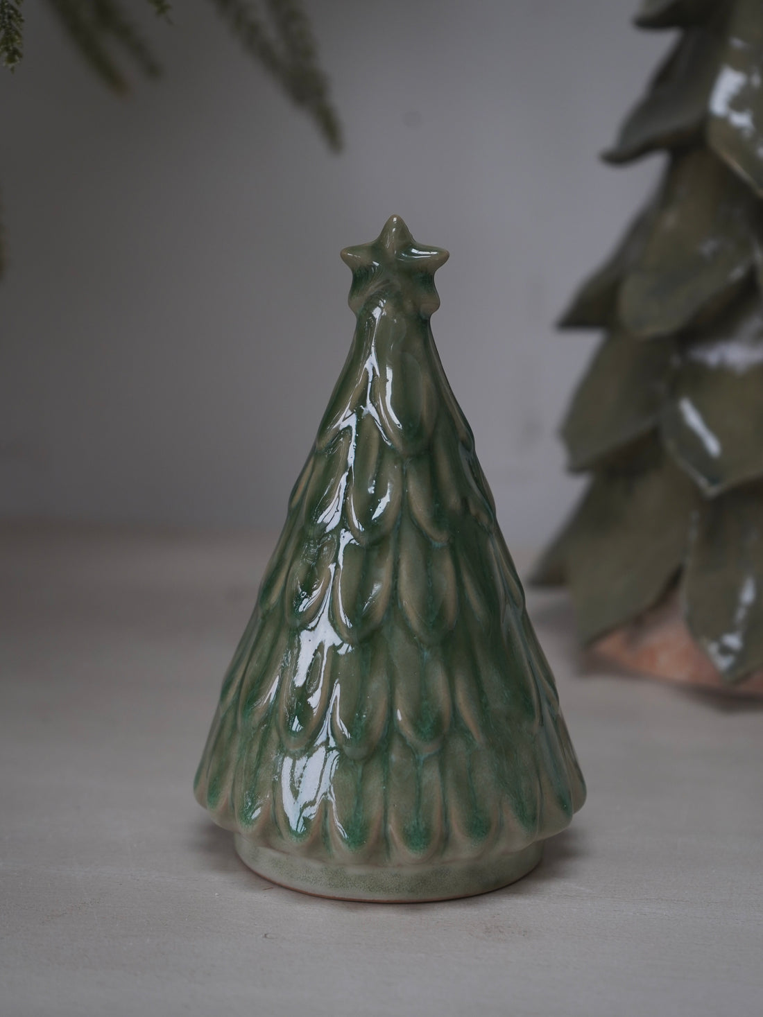 Green ceramic Christmas tree ornament on a neutral background