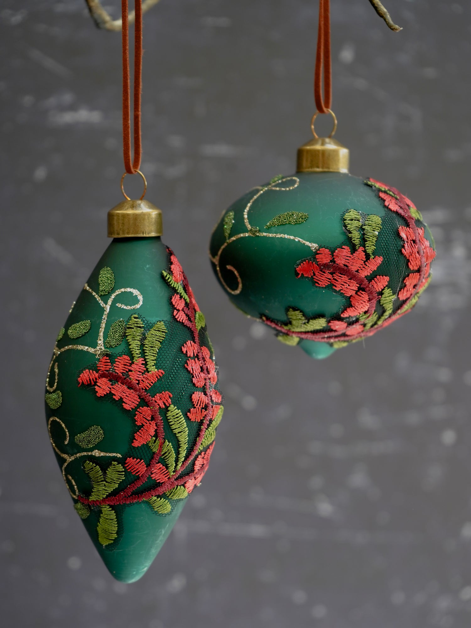 Two green embroidered ornaments hanging against a dark background