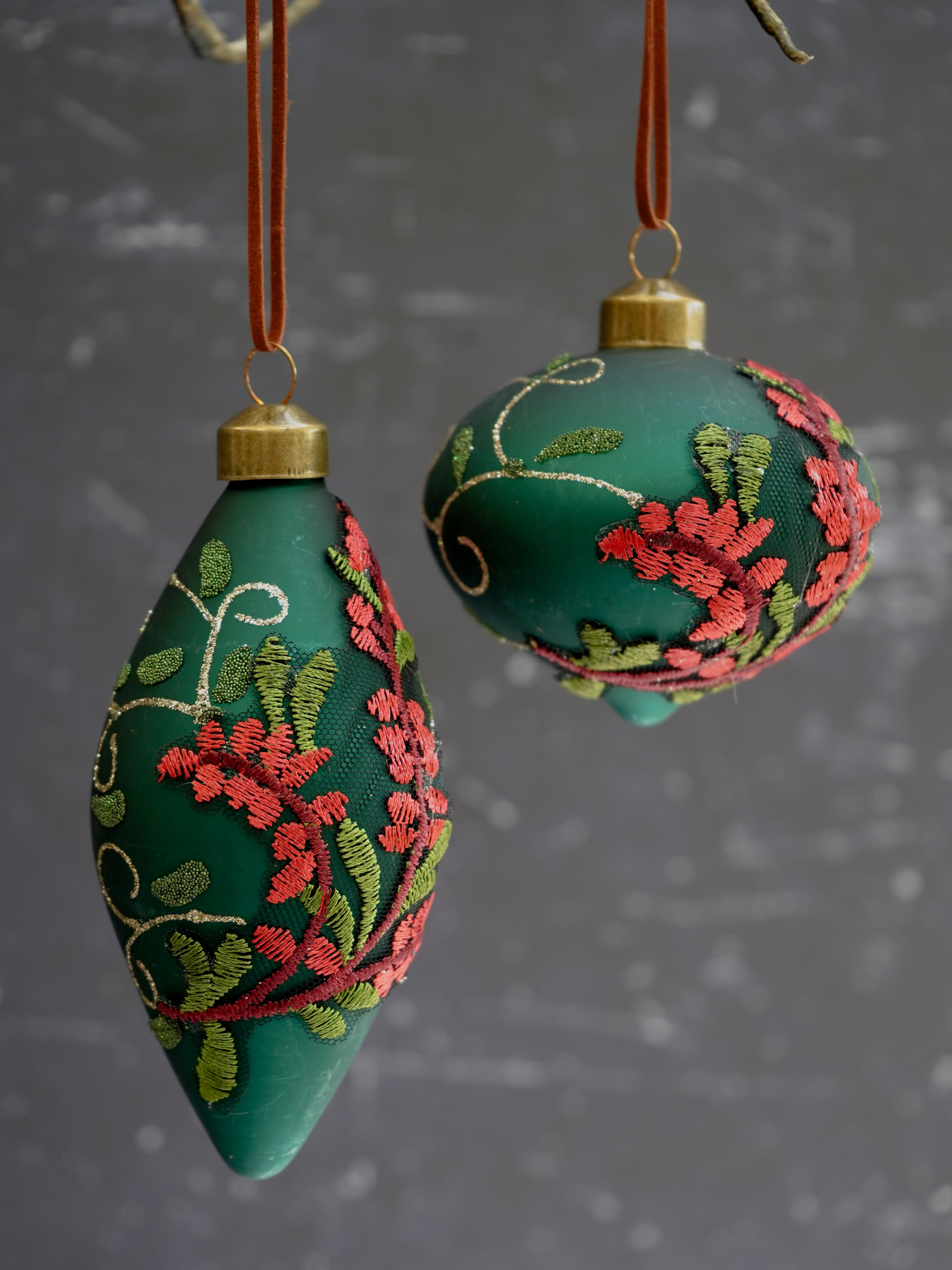 Two green embroidered ornaments hanging against a dark background