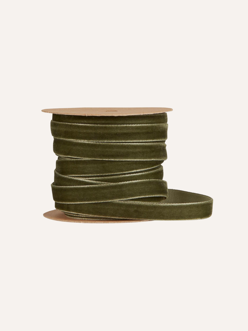 Spool of moss green velvet ribbon on a beige background